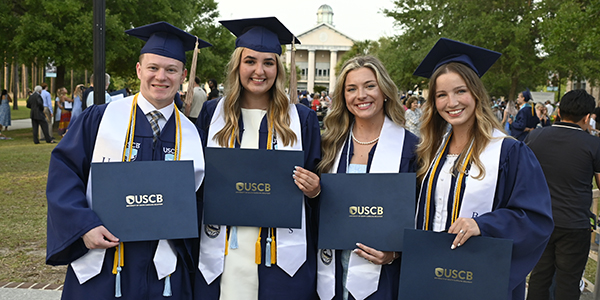 Four graduates in caps and gowns Four graduates in caps and gowns